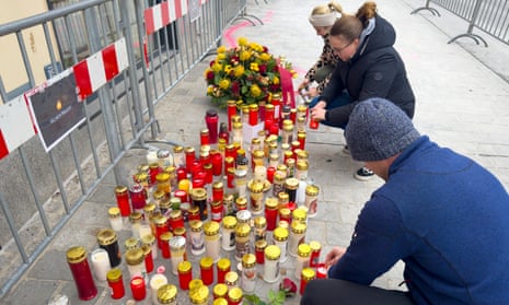 People kneel to light candles beside a temporary metal fence