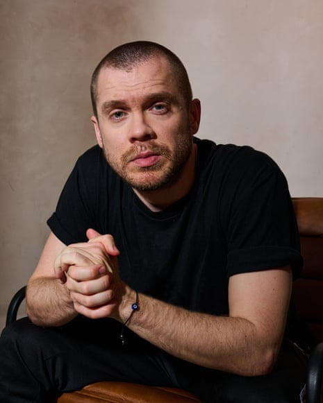 A man in a black T-shirt with a closely-shaved head looking directly at the camera