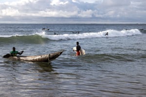 A surfer with a broken board enters the water next to a pirogue in Robertsport