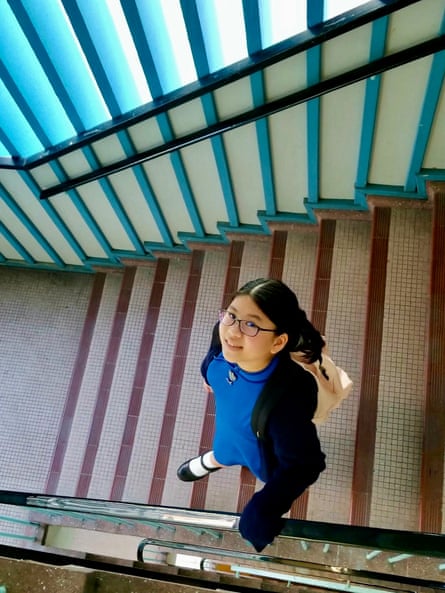 Luna wearing school uniform, looking up at the camera, smiling, as she walks down a staircase inside a building