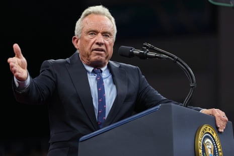 RFK Jr, wearing a suit, speaks into a microphone with hand gestured at lectern