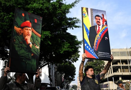 Two people hold up large placards bearing the images of Hugo Chávez and Nicolás Maduro