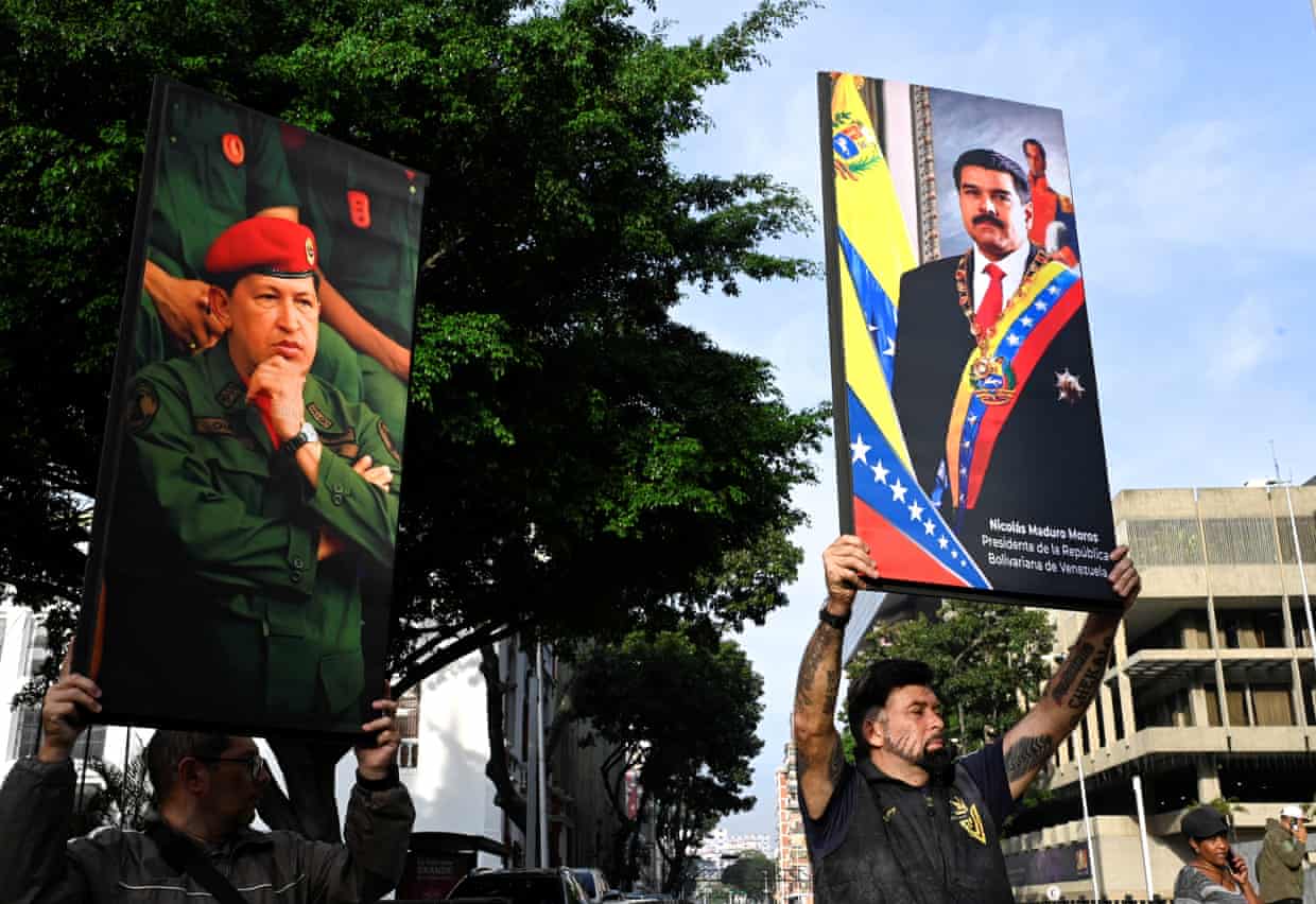 Two people hold up large placards bearing the images of Hugo Chávez and Nicolás Maduro