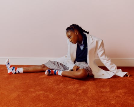 Musician Little Simz sitting on the floor, one leg outstretched in front of her