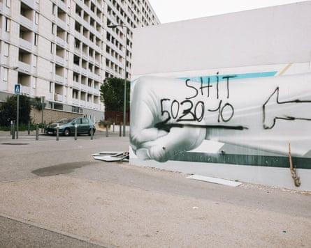 A mural of a clenched fist is defaced with black spray-painted “SHIT” graffiti and numbers, beside an apartment block