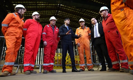 Rishi Sunak and Douglas Ross standing in a semicircle with people wearing orange or red overalls and hard hats in front of a warehouse