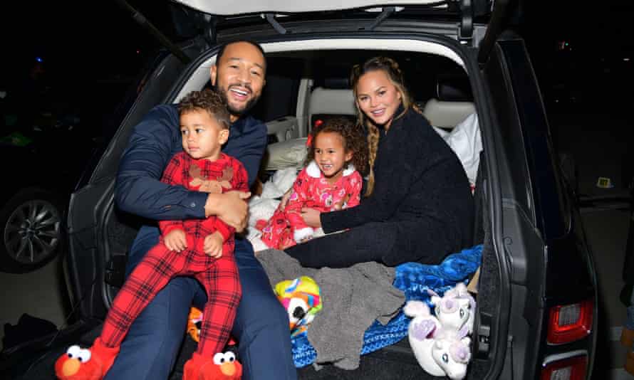A family of two adults and two children smiles for the camera while sitting in the trunk of their car.