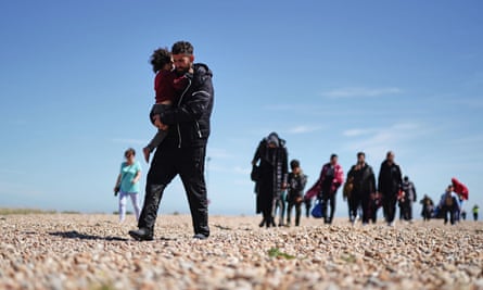 Migrants walk on a beach in Dungeness, Kent. They include men, women and children