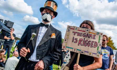A protester is dressed like a rich man and another with a banner reading ‘the game is rigged’ 