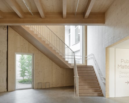 A plywood staircase ascends beside a glass door, inside Design Museum Ghent