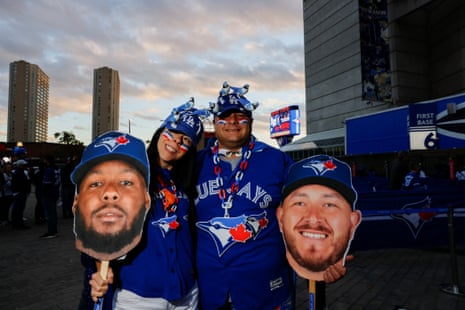 A pair of Toronto fans, wearing LA hats with Blue Jay figures simulating to defacte on them, stand holding cardboard cut outs of Alejandro Kirk and Vladimir Guerrero Jr before Game 7.