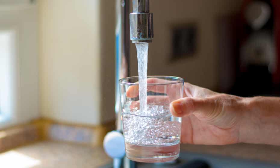 Woman filling a glass of water from a stainless steel or chrome tap or faucet