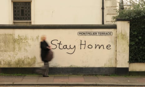 A woman passes a wall with 'stay home' painted on it