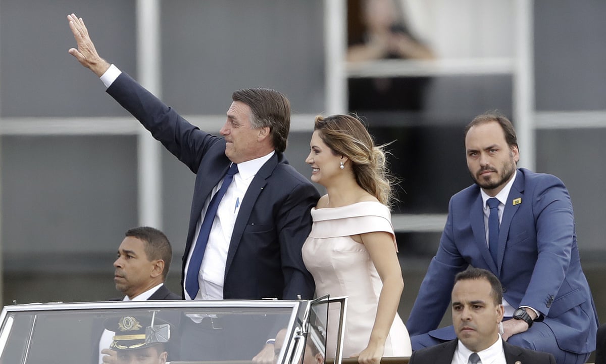 From left, Jair, Michelle and Carlos Bolsonaro riding in an open car after Jair Bolsonaro’s swearing in ceremony in 2019.