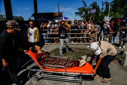 An unconscious Filipina is carried away on a stretcher as people queue in hot sun behind them