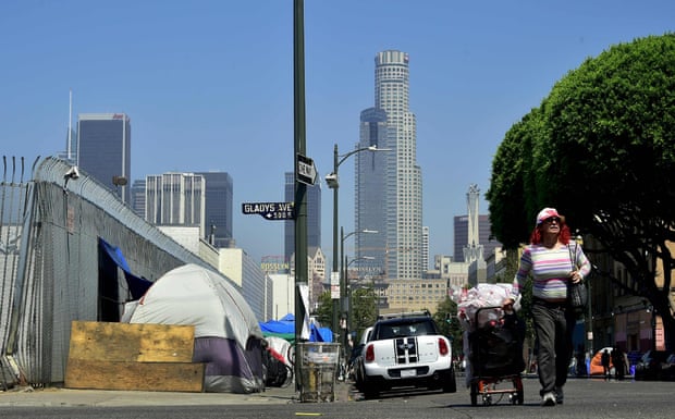 A woman pushes a cart full of her belongings past tents near Skid Row in downtown Los Angeles.