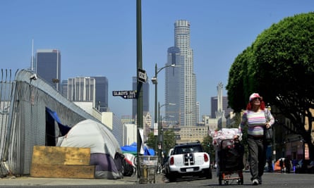 A woman pushes a cart full of belongings past tents on the sidewalk near Skid Row in downtown Los Angeles.