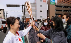 Spectators touch the torch carried by torchbearer Junko Ito, on the second day of the Olympic torch relay in Fukushima, Japan 26 March, 2021.
