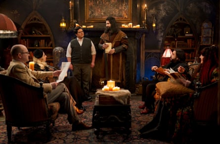 Nandor and Guillermo stood by a fireplace with the other vampires seated around