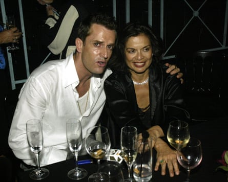 The pair sit at a bar table covered in empty glasses, he with his arm around her shoulders
