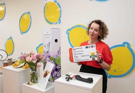 A woman posing with a novelty-sized Qantas boarding pass and landline phone in front of a white wall covered in giant lemon stickers