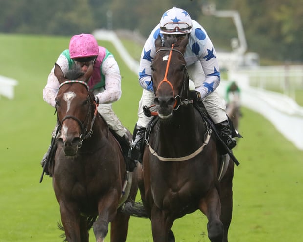 Two race horses, one with a jockey in a pink cap, the other one in white with blue stars