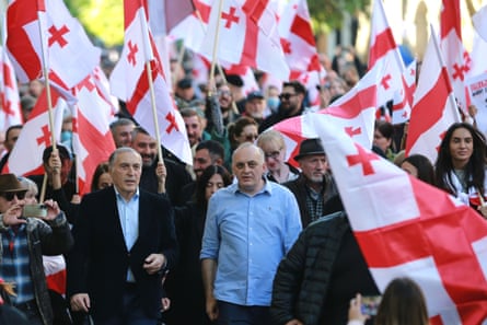 Burchuladze, who is 70 and has grey hair, walks among a crowd of people of all ages, many of whom are holding red and white Georgian flags