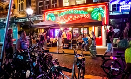 A crowd of young people and lots of bicycles outside a cannabis/coffee shop