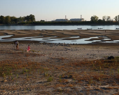 people walk on dried up river bed in front of a nuclear power plant