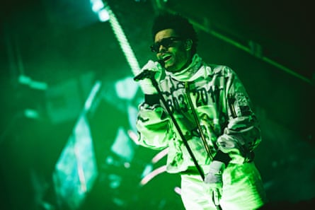 Tesfaye singing into a mic on stage, lit in green