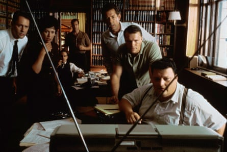 seven people gathered in a 60s office around a TV, looking shocked, in the film JFK
