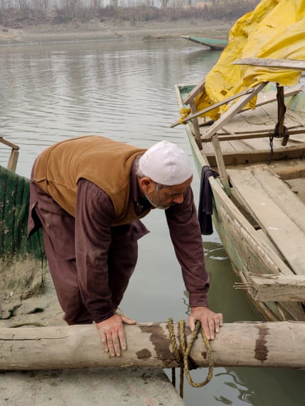 Dar bends over a log, which has been placed to bridge the gap between dry land and his boat.