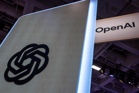 A close-up of a wooden OpenAI logo sign beside an illuminated OpenAI banner at a conference venue