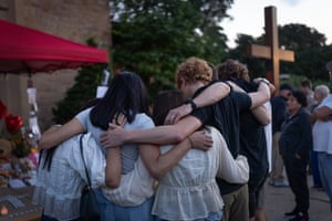 People stand together with their arms around each other's shoulders and their heads bowed