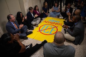 people clap and chant while seated on the floor around a banner that reads ‘New Yorkers against ice’