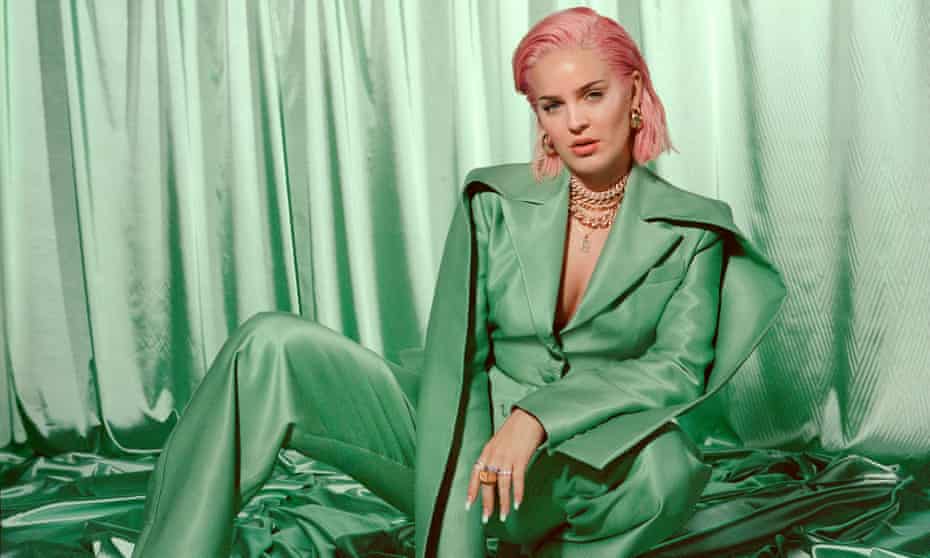 Anne-Marie in a bright green satin trouser suit and cape, pink hair and several chunky gold necklaces