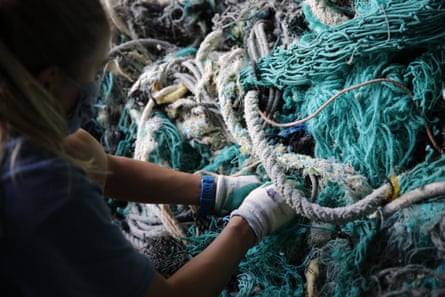 A woman in rubber gloves in front of a enormous knot of ropes and nets