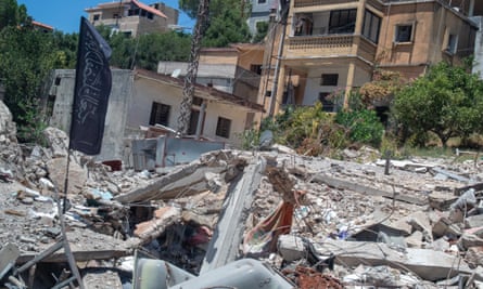 A black flag with Arabic writing on it, placed on a pile of rubble, with housing in the background