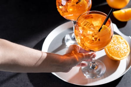 Closeup of a woman's hand holding an Aperol Spritz cocktail served with ice cubes, orange slices, and a black straw.