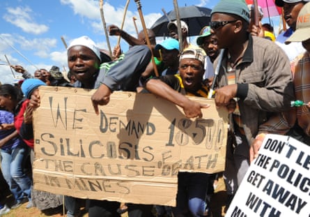 Striking miners hold a sign calling for silicosis payouts