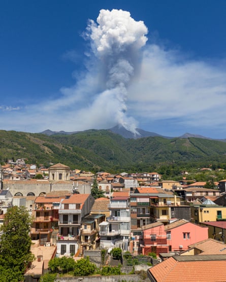Mount Edna spewing ash in the background, with a town of houses in front