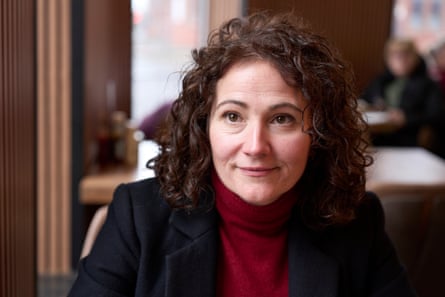 Angeliki Stogia in red polo neck and blue jacket in a cafe