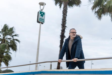 A man leans on a railing outside next to a tsunami warning sign