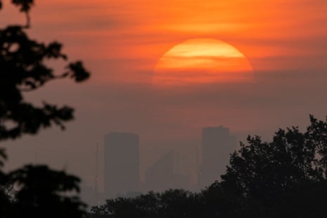 The golden sun rising in the sky behind low cloud over London, viewed from a park