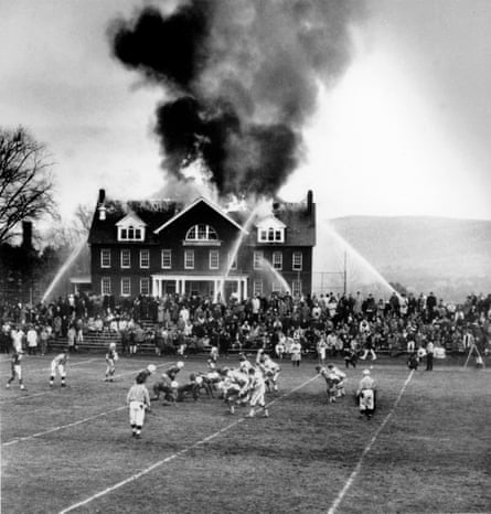 Spectators divide their attention as the Mount Hermon, Mass. High School football team hosts Deerfield Academy during a structure fire in the Mount Hermon science building Nov. 24, 1965. The science building was destroyed, and Mount Hermon lost the football game, ending a two-year-long winning streak