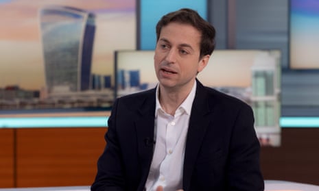 Gideon Falter speaking in studio on the Good Morning Britain' TV show, 22 Apr 2024: he wears a dark jacket and open-necked white shirt and is seen against a backdrop of screens and images of London skyscrapers