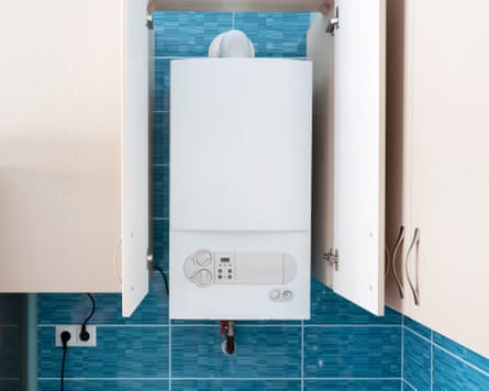 A white gas boiler mounted in a wall cupboard. The cupboard door is open to show the boiler