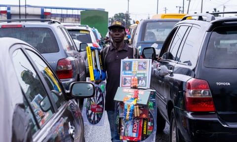 A man stands beywee lines of cars hawking goods