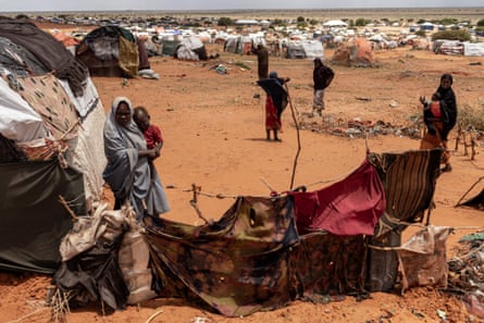 A woman holds a child next to a tent in a camp for displaced people in Somalia.