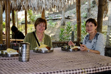 Two women at a table outdoors eating an Indian thali but smiling at camera